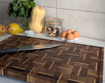 Könnte beinhalten: Rechteckiges Holzschneidebrett mit einem geometrischen Muster aus dunklem und hellem Holz. Ein Edelstahlmesser liegt auf dem Brett. Das Brett ist von frischen Produkten und Eiern umgeben.