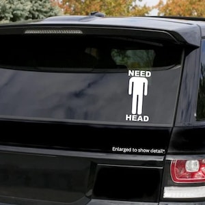May include: White vinyl sticker with a stick figure and the words "NEED HEAD" on a black car.