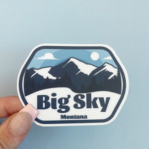May include: A white sticker with a blue and white mountain scene and the text "Big Sky Montana".