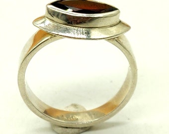 May include: A silver ring with a dark red gemstone set in a unique, modern design.