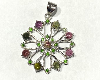 May include: A silver pendant featuring a flower design with green and pink gemstones. The pendant has a bail for attaching to a chain.