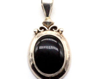 May include: A silver pendant with an oval black gemstone set in a silver bezel. The pendant has a decorative bail with a scroll design.