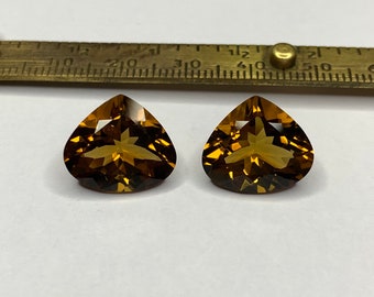 May include: Two heart-shaped, faceted gemstones with a golden brown color. The gemstones are set against a white background.