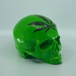 May include: A green human skull with a black marijuana leaf design on the top of the head.