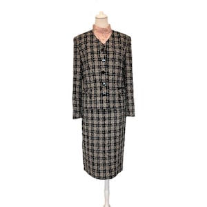 Könnte beinhalten: Ein zweiteiliges Vintage-Anzug-Set, bestehend aus einer Jacke und einem knielangen Rock. Der Anzug ist aus einem schwarz-beige karierten Tweedstoff gefertigt. Die Jacke hat eine Knopfleiste und eine hellrosa Bluse darunter.