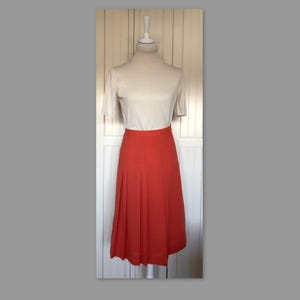 Könnte beinhalten: Ein korallenfarbener Faltenrock mit hoher Taille und knielangem Saum.