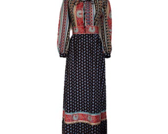 May include: A vintage maxi dress with a colorful paisley pattern. The dress features long sleeves, a round neckline, and a fitted waist. The skirt is black with a repeating blue and white floral design, and the bodice has red, black, and gold accents.
