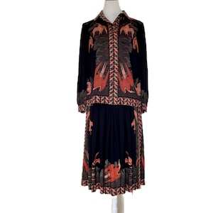 Könnte beinhalten: Ein marineblaues Vintage-Kleid mit langen Ärmeln und einem Kragen. Das Kleid hat ein sich wiederholendes Muster aus orangefarbenen und braunen Vögeln und geometrischen Formen. Das Kleid wird auf einer weißen Schaufeniquin präsentiert.