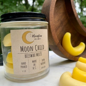 May include: A glass jar filled with yellow beeswax melts labeled "Moon Child Beeswax Melts". The label also states "Hand Poured", "Made in N.C.", "100% Natural", and "Batch #1".