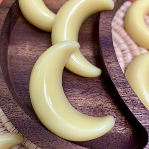 May include: A wooden tray with a crescent moon shape holds multiple small, pale yellow, crescent moon-shaped wax melts.