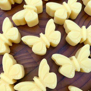 May include: A collection of 12 small, yellow butterfly-shaped soaps on a wooden surface. The soaps are all the same size and shape, and they have a smooth, glossy finish.