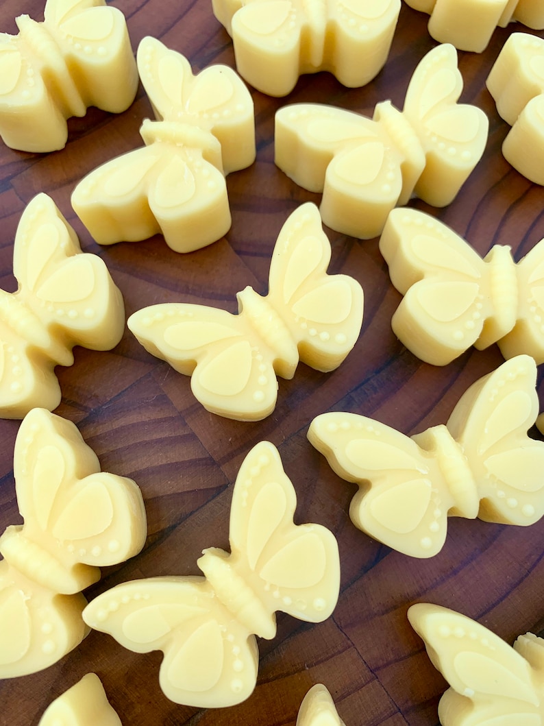 May include: A collection of 12 small, yellow butterfly-shaped soaps on a wooden surface. The soaps are all the same size and shape, and they have a smooth, glossy finish.