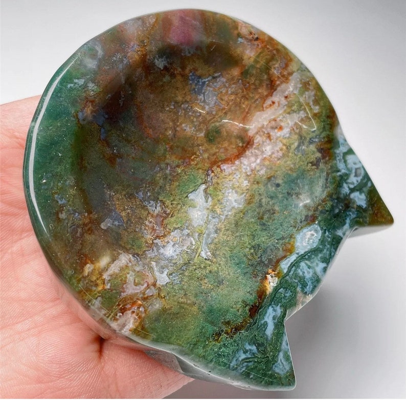 May include: A green, brown and white agate cat dish. The dish is carved from a single piece of agate and has a natural, organic shape.
