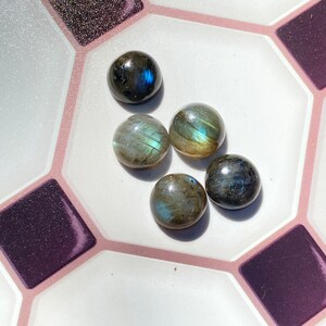 May include: Five round, iridescent, gray and blue labradorite gemstones on a white and pink tiled surface.