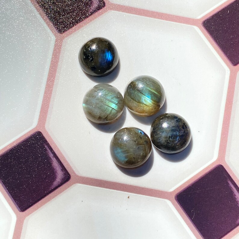 May include: Five round, iridescent, gray and blue labradorite gemstones on a white and pink tiled surface.
