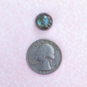 May include: A round, iridescent, gray and blue gemstone cabochon. The gemstone is about the size of a US quarter.