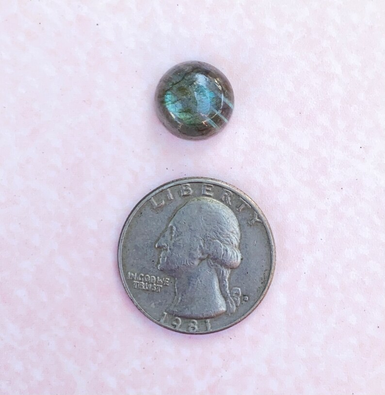 May include: A round, iridescent, gray and blue gemstone cabochon. The gemstone is about the size of a US quarter.