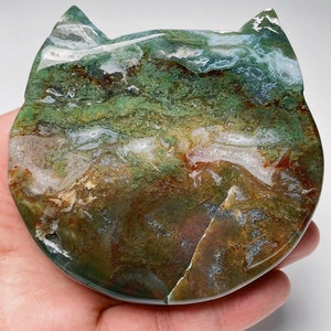 May include: A green, brown and white agate stone carved into the shape of a cat. The stone has a swirling pattern and is polished smooth.