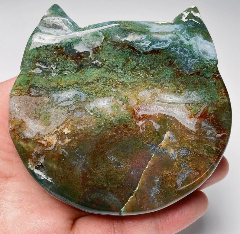 May include: A green, brown and white agate stone carved into the shape of a cat. The stone has a swirling pattern and is polished smooth.