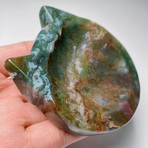 May include: A green, brown and white agate stone carved into the shape of a cat's head. The stone has a natural, polished finish and is ideal for holding small items.