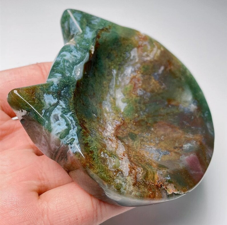 May include: A green, brown and white agate stone carved into the shape of a cat's head. The stone has a natural, polished finish and is ideal for holding small items.