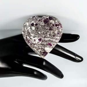 May include: A heart-shaped stone with a white and gray base and purple and red flecks throughout.