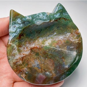 May include: A green, brown and white agate cat dish. The dish is carved in the shape of a cat's head and has a smooth, polished surface.