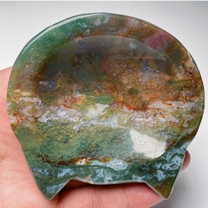 May include: A green, brown and white agate dish with a scalloped edge. The dish is made from natural stone and has a unique, organic shape.