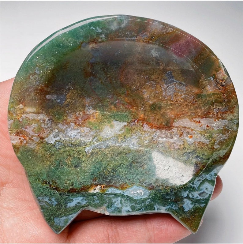 May include: A green, brown and white agate dish with a scalloped edge. The dish is made from natural stone and has a unique, organic shape.