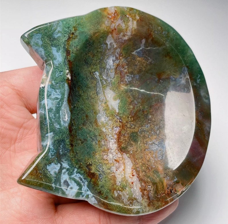May include: A green, brown, and white agate stone carved into a cat-shaped dish. The dish has a smooth, polished surface and a shallow bowl.