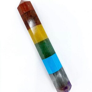 May include: A seven chakra crystal wand with a pointed tip. The wand is made of seven different colored stones, starting with red at the top and ending with purple at the bottom. The colors are red, orange, yellow, green, blue, indigo, and violet.