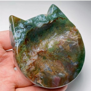 May include: Green, brown, and white agate stone carved into the shape of a cat's head. The stone has a natural, polished finish.