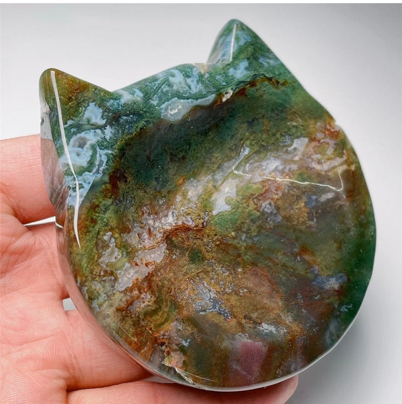 May include: Green, brown, and white agate stone carved into the shape of a cat's head. The stone has a natural, polished finish.