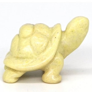 May include: A small, pale yellow, carved turtle figurine. The turtle is walking with its head raised.
