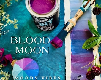 May include: An open can of deep purple paint, a paintbrush, and a painted ornament are displayed on a teal surface. The words "BLOOD MOON" and "MOODY VIBES" are printed on the surface. The paintbrush has a wooden handle and a dark purple tip. Berries and leaves are also present.