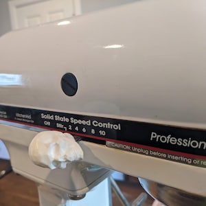 May include: White stand mixer with a black control panel labeled "Solid State Speed Control" and "Professional". The control panel has a dial with numbers 2, 4, 6, 8, and 10. The mixer has a white knob with a black center.