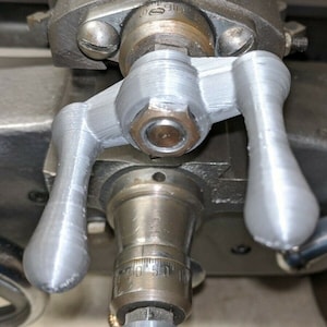 May include: Close-up of a silver metal machine part with two gray 3D printed levers. The levers are attached to a round metal shaft with a silver nut. The shaft has a circular dial with numbers 0 to 50.