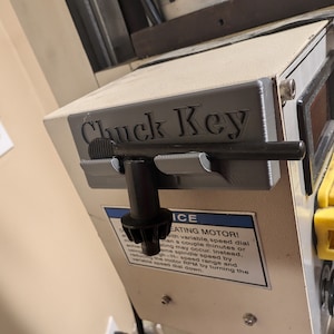 May include: A close-up of a gray metal box with the words "Chuck Key" printed on it. The box is attached to a larger piece of machinery.