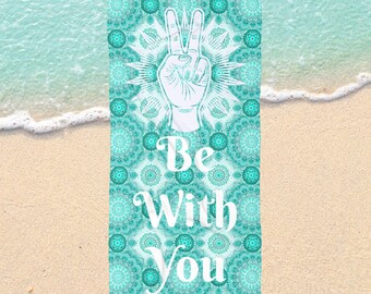 Könnte beinhalten: Ein rechteckiges Strandtuch mit einem türkisfarbenen Mandala-Muster und den Worten "Be With You" in Weiß. Eine weiße Hand mit Friedenszeichen befindet sich in der Mitte. Das Tuch liegt auf einem Sandstrand mit Wellen.