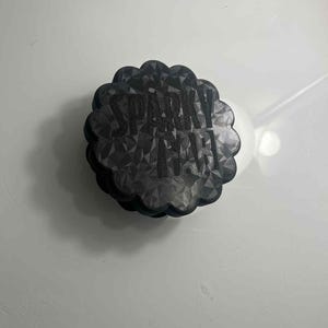 Peut inclure: Un dessous de verre noir, à bord festonné, avec un motif géométrique et le texte "SPARKLE" en blanc. Le dessous de verre est rond et semble être fait d'un matériau texturé.