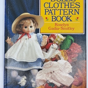 May include: A book titled "Dolls' Clothes Pattern Book" by Roselyn Gadia-Smitley. The cover features a doll wearing a blue and white gingham dress and a straw hat. The doll is surrounded by fabric scraps and sewing supplies.