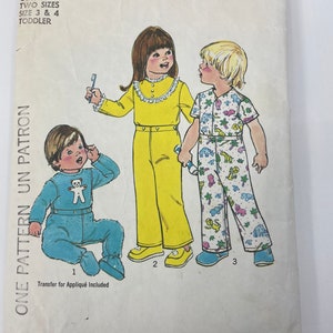 May include: Simplicity sewing pattern number 7067 for toddler pyjamas. The pattern includes three different styles: a blue jumpsuit with a teddy bear appliqué, a yellow jumpsuit with a lace trim, and a multi-coloured jumpsuit with a jungle animal print. The pattern includes instructions for sizes 3 and 4.