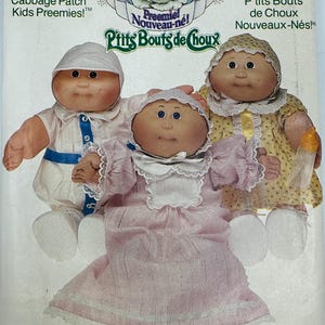 May include: A Butterick sewing pattern envelope 6980 for Cabbage Patch Kids Preemies clothes. The cover features three dolls wearing handmade outfits: a white romper with a blue sash, a pink dress with a white lace collar, and a yellow floral dress.