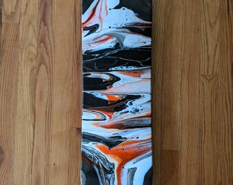 May include: A black, white, and orange skateboard deck with a marbled paint design.