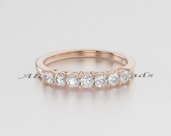 May include: Rose gold band ring featuring a row of seven round, clear gemstones. The ring is set on a white surface, with the gemstones catching the light. The ring's design is simple and elegant, suitable for everyday wear or special occasions.