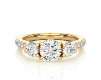 May include: A gold ring featuring three large, round, clear gemstones at the centre, with smaller, clear gemstones set along the band. The ring is set against a white background.