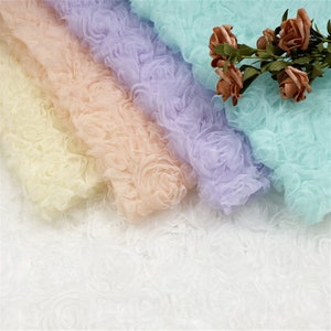 May include: Four layers of tulle fabric in pastel colors, including light yellow, peach, lavender, and light blue. The fabric has a 3D rose pattern and is arranged in a cascading effect.