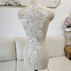 May include: White lace applique with floral designs. The lace is delicate and intricate, with a variety of flower shapes and sizes. The applique is perfect for adding a touch of elegance to any garment.