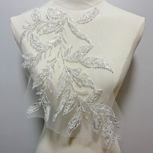 May include: White beaded floral applique with a delicate design. The applique is made of sequins and beads and is perfect for adding a touch of elegance to any garment.