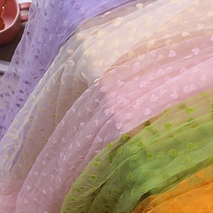 Op de afbeelding: Een stapel doorschijnende stof met een hartjespatroon in verschillende kleuren, waaronder paars, roze, groen en oranje.
